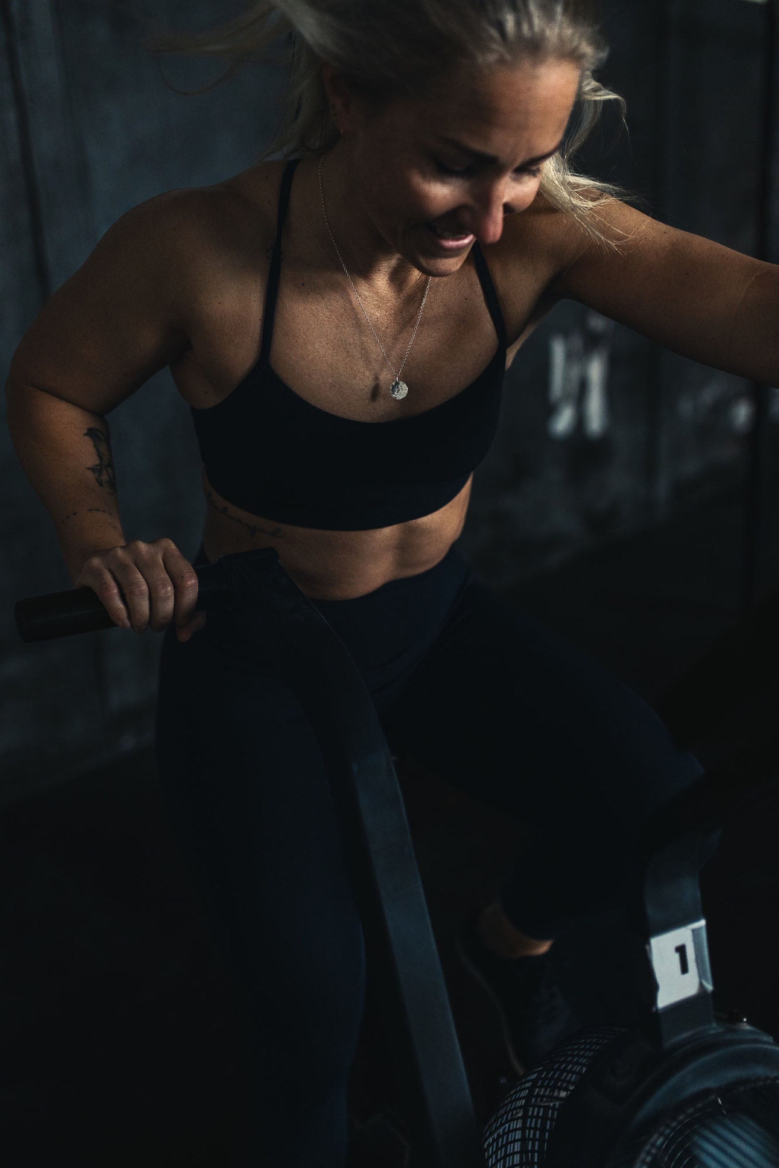 Smiling athlete pushing through an air bike interval in a Movement Rebels session, lit by warm window light