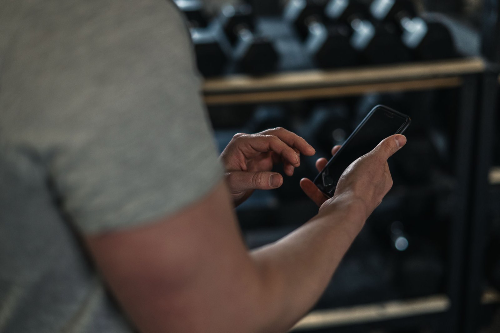 Athlete checking his training plan on his phone by the dumbbell rack in the Movement Rebels coaching app
