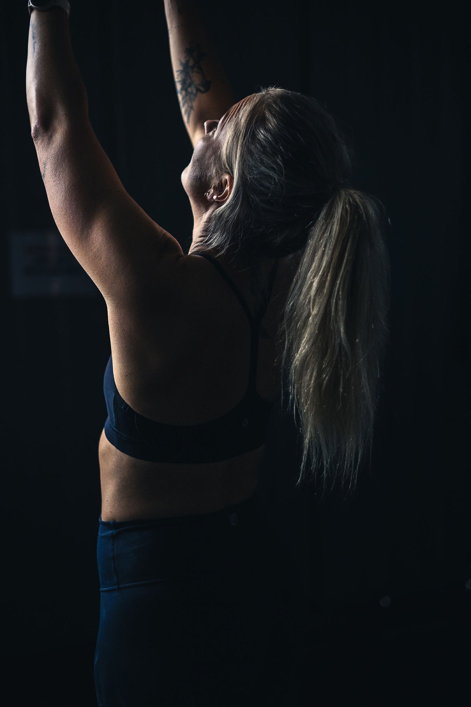 Female athlete reaching for the pull-up bar in a dark gym, wearing the sports watch that syncs with Movement Rebels