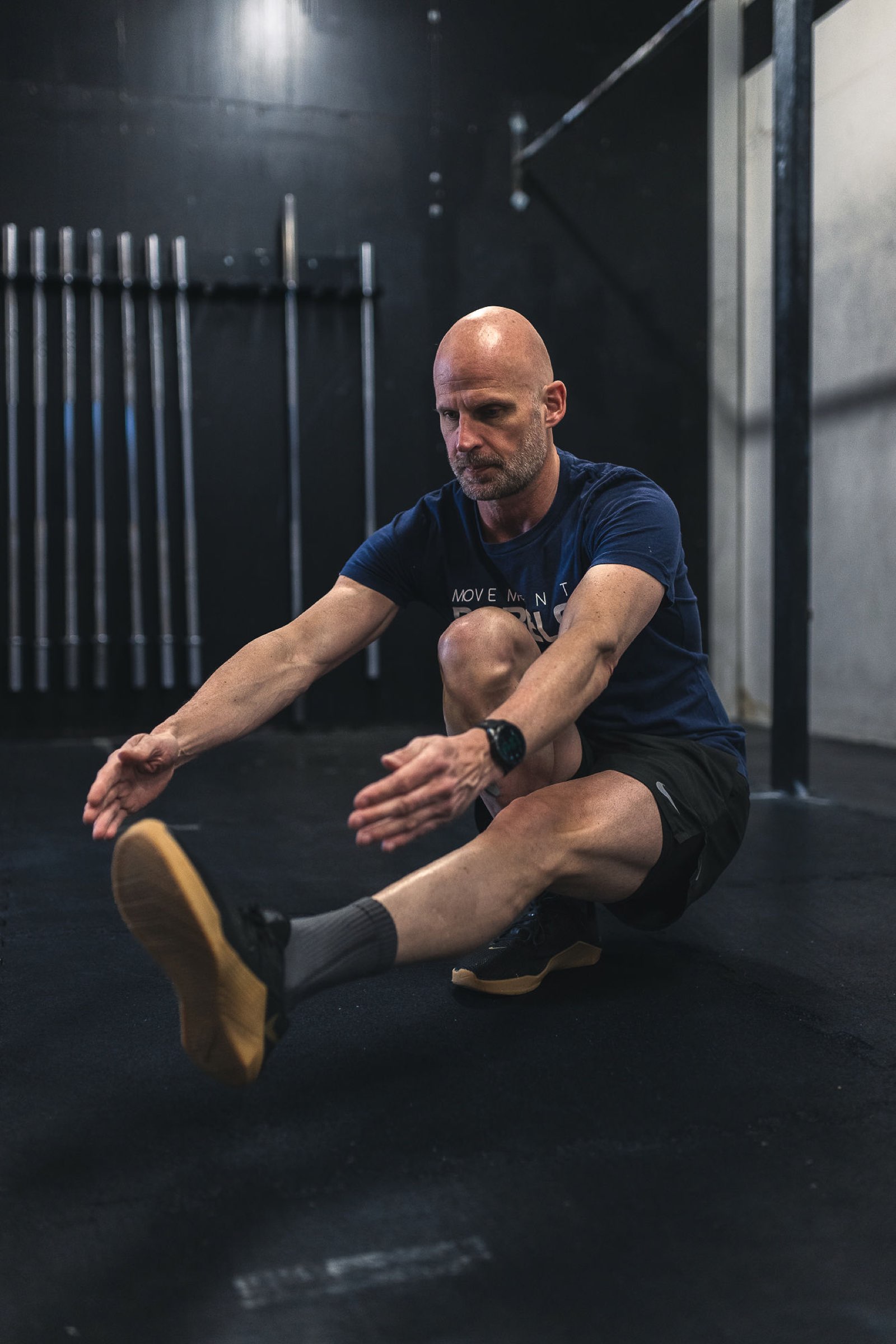 Masters athlete in a Movement Rebels shirt balancing a pistol squat in a dark gym