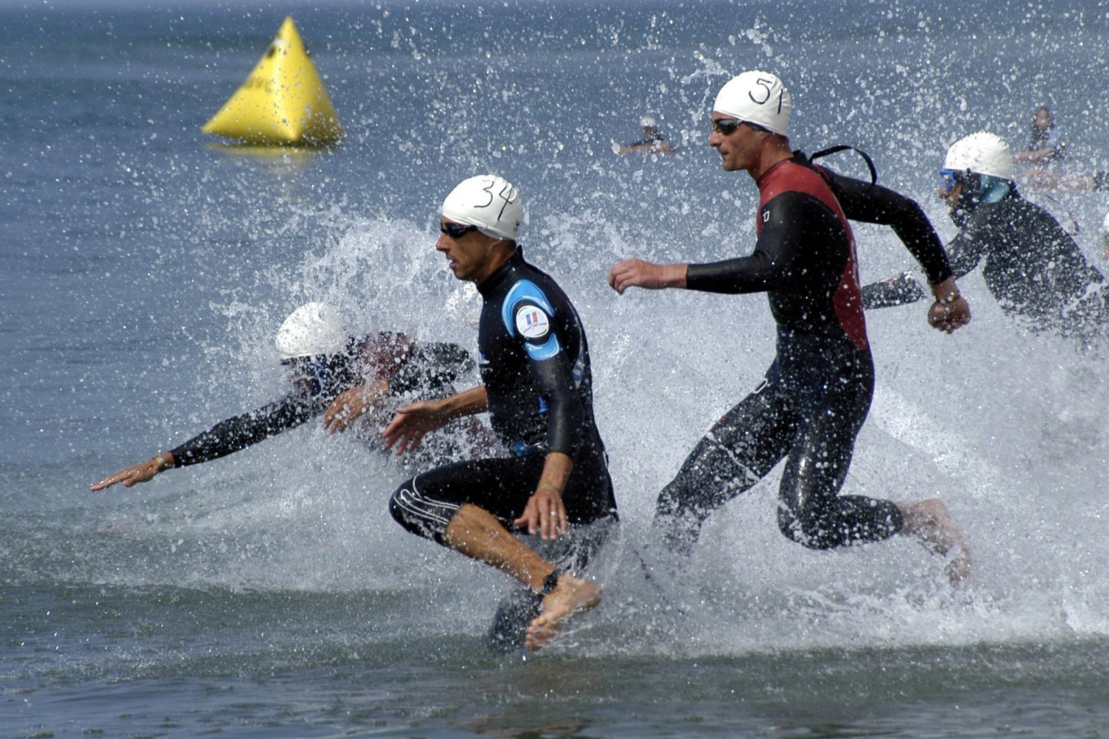Triathletes in wetsuits and numbered swim caps running into the sea at a race swim start
